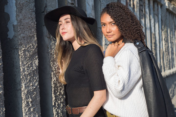 Portrait of a pair of beautiful fashionable Spanish girls standing against a texture wall. Fashion photography Street art