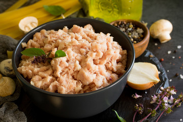 Fresh minced meat close-up and ingredients for cooking - mushrooms, pasta, spices and eggs on a dark stone countertop.