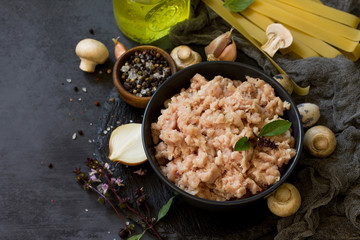Fresh minced meat and ingredients for cooking - mushrooms, pasta, spices and eggs on a dark stone countertop. Copy space.