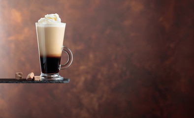 Coffee cocktail with cream and pieces of brown sugar on a brown background.