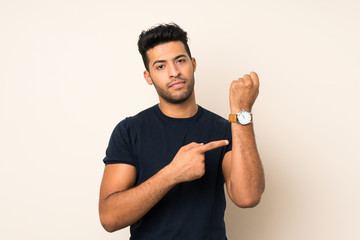 Young handsome man over isolated background showing the hand watch with serious expression serious...