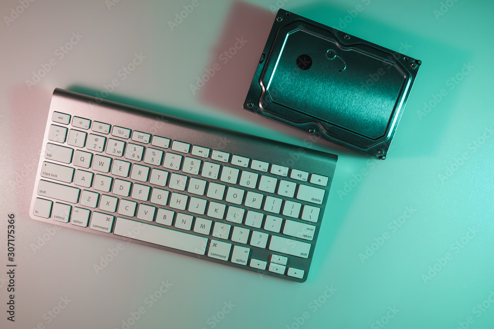 Aufkleber Beautiful modern silver keyboard and hard disk in the color light on a table night background. Top view.