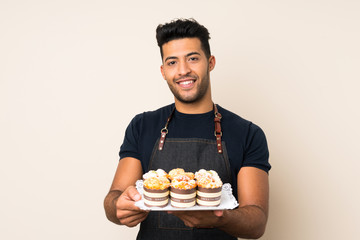 Young handsome man over isolated background holding mini cakes