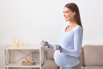 Side view of pregnant girl lifting blue dumbbells