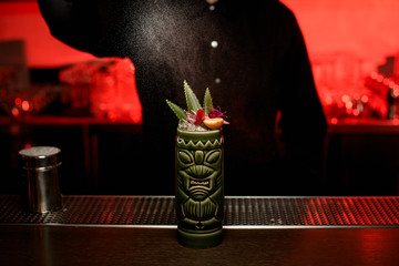 Bartender girl serving alcoholic cocktail in the Tiki mug sprinkling on it with sugar powder