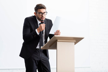 scared businessman in suit standing at podium tribune and speaking during conference isolated on white