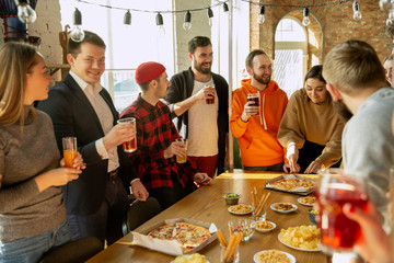 Happy co-workers celebrating while company party and corporate event. Young caucasian people in casual clothes drinking, laughting. Concept of office culture, teamwork, friendship, holidays, weekend.