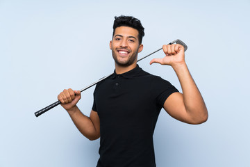 Handsome young man playing golf over isolated blue background proud and self-satisfied