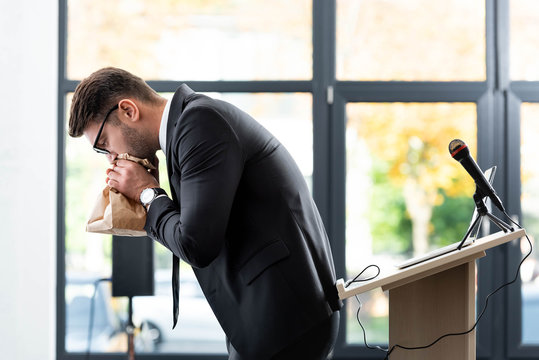 side view of scared businessman in suit breathing in paper bag during conference