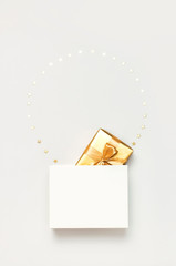 Beautiful golden gift white paper bag confetti stars on gray background top view Flat lay. New Year presents Festive decorations 2020 celebration. Merry Christmas Happy Holidays card