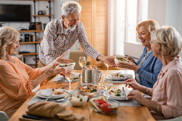 Happy senior man serving lunch to his friends at dining table.