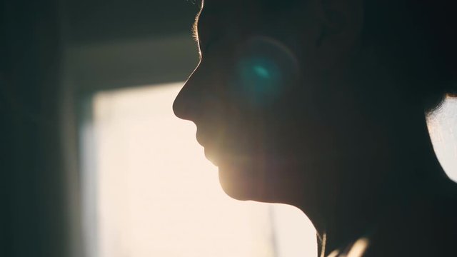 CU: dark silhouette of young woman using inhaler to relief asthma symptom against backlight in room extreme close view