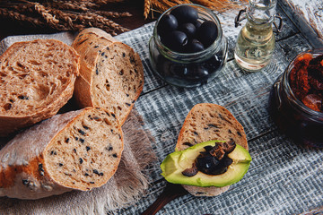 Healthy rye wholegrain bread with olives, avocado and sun-dried tomatoes on a wooden farmer's table. Homemade cake. traditional Italian food