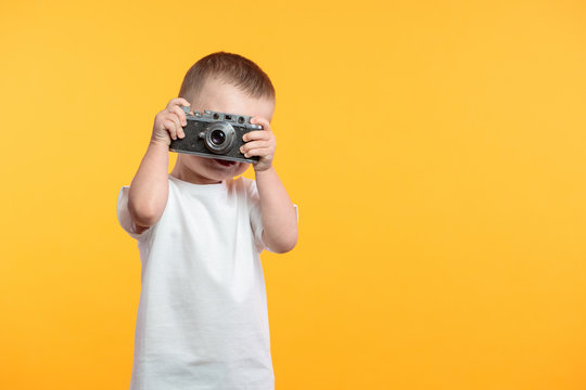 Boy taking a picture with a retro camera over yellow background