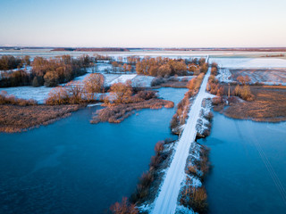Fototapeta na wymiar Aerial view of lake and snow covered bridge over it during nice sunrise in Lithuania - Winter landscape