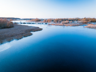 Calm lake on cold winter morning with bridge in background - first winter snow in Lithuania