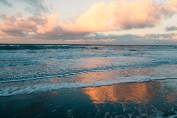 Ostseestrand mit Wellen, Gischt bei Sonnenuntergang mit rotgelb leuchtenden Wolken im Winter