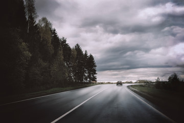 Moody landscape with dark storm clouds, forest, car and road out of horizon. Beautiful nature background and wallpaper