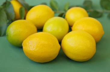 A pile of juicy lemons with green leaves on a green background. Organic citrus fruits for a healthy diet. Close-up.