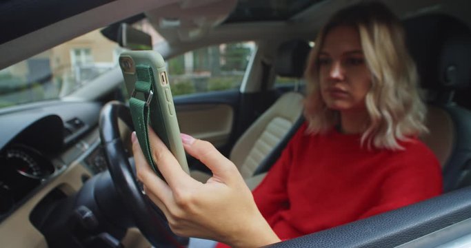 Closeup of young female hands using smartphone in car driver seat. Blonde wtylish woman chatting online. Driving courses online. Map application. Traveling abroad. Social networking. Notification