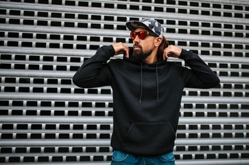 City portrait of handsome hipster guy with beard wearing black blank hoodie or hoody with space for...