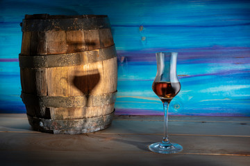 A glass of Grappa next to the oak barrel on a blue background