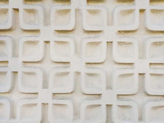 Close-up picture of geometric stucco work on an exterior wall. Light beige plaster pattern. Architectural detail in soft light