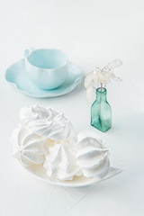 Fototapeta na wymiar A delicate white handmade meringue next to a blue tea Cup stands on a light background. Close up. Copy space