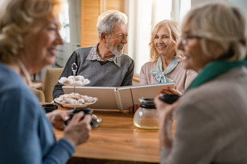 Happy senior couple talking while looking at photo album at home.