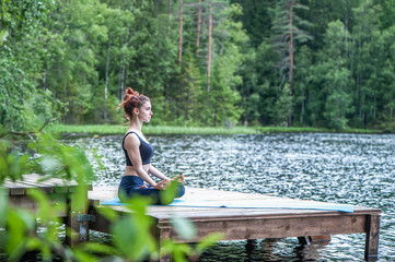 Fototapeta na wymiar Young girl practicing yoga in the nature on the lake. Female happiness. Landscape background