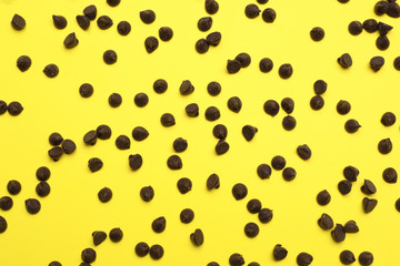 Delicious chocolate chips on yellow background, top view