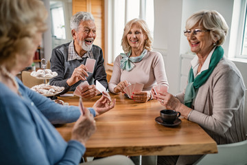 Group of cheerful seniors playing cards during coffee time at home.