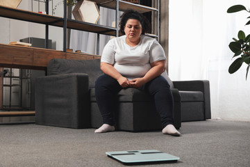 Depressed overweight woman looking at scales in living room