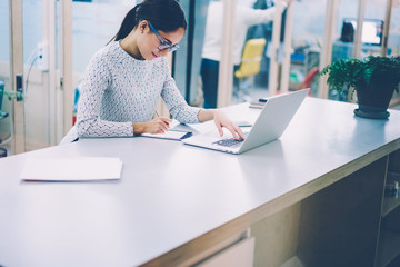 Concentrated female designer drawing using modern technologies on tablet connected to netbook in...