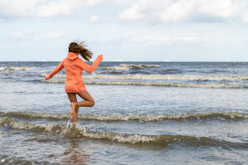 Fototapeta na wymiar junges mädchen hüpft am strand in den wellen bei wolkenhimmel