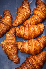 Fresh croissants with crumbs on a blue background on the bakery counter.