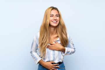 Young blonde woman over isolated blue background smiling a lot