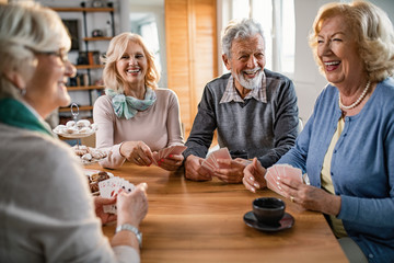 Group of happy seniors laughing while playing cards together at home.