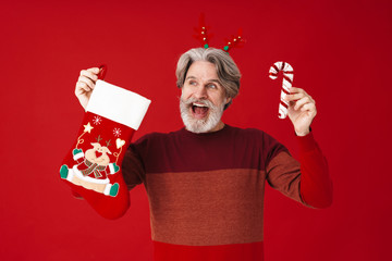 Portrait of bearded old man holding candy cane and Christmas gift sock