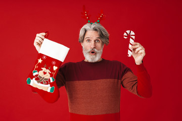 Portrait of bearded old man holding candy cane and Christmas gift sock