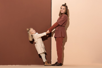side view of smiling daughter and mother holding hands on beige and brown background