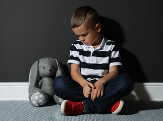Sad little boy with toy near black wall. Domestic violence concept