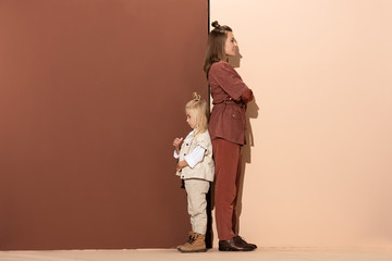 back to back view of daughter and smiling mother on beige and brown background