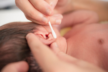 Mother hands cleaning ear of newborn baby  with cotton