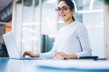 Portrait of skilled administrative assistant of office satisfied with occupation using laptop...