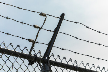 low angle view of the exterior electric fence with barbed wire on the top, in high-voltage electrical substation against the sky, with copy space