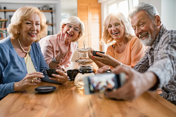 Happy mature friends taking selfie and having fun gathering at home.