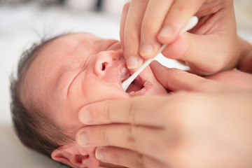 Mother cleaning baby nose with cotton swab while infant lying on bed
