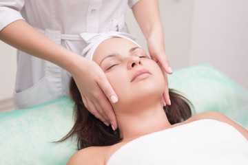 Girl massage therapist does facial massage with a beautiful woman. Hands are closing. Massage room