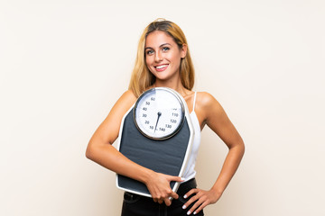 Young blonde woman with weighing machine over isolated background